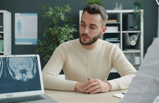 Man sitting across from a doctor with a brain MRI scan displayed on a laptop during a consultation at a memory & brain health hospital