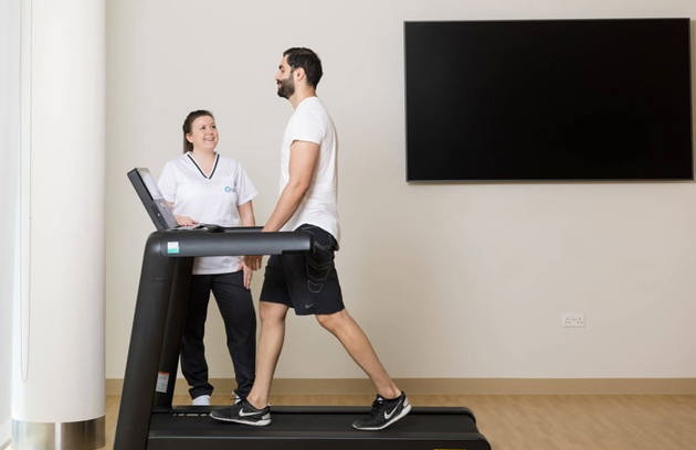 A man walks on a treadmill, assisted by a Mubadala Health Dubai worker.
